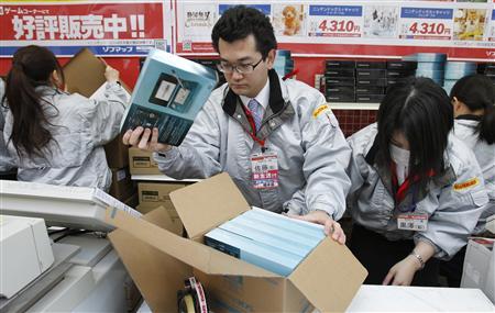 Сотрудники магазина электроники распаковывают новые игровые консоли 3DS во время запуска в Токио